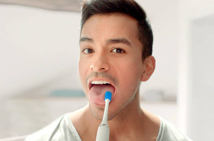 En man kigger mod kameraet, mens han reng&oslash;r sin tunge med en tungeb&oslash;rste fra Philips.